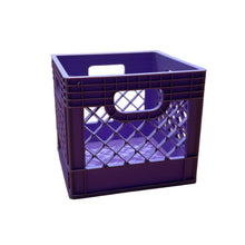A small purple plastic crate with cutout sides and handle holes sits on a wooden tabletop in a store setting, with a blurred person and store fixtures in the background.